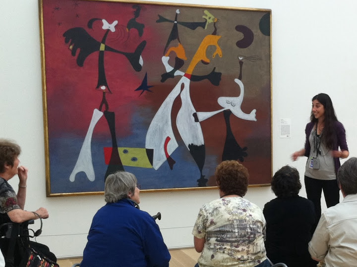 Kate standing in front of a painting by Miro in an art gallery, teaching a group of students